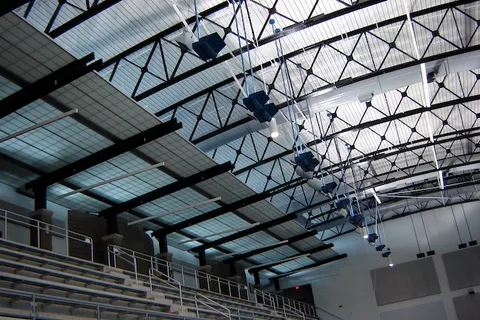 Painted steel roof trusses and bleacher seating inside an indoor athletic facility