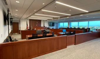 Courtroom with cherry-stained wood millwork, carpeted floor, and a row of windows