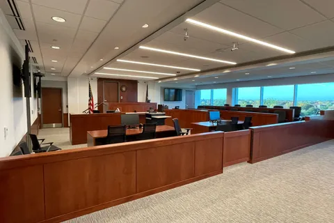 Courtroom with cherry-stained wood millwork, carpeted floor, and a row of windows