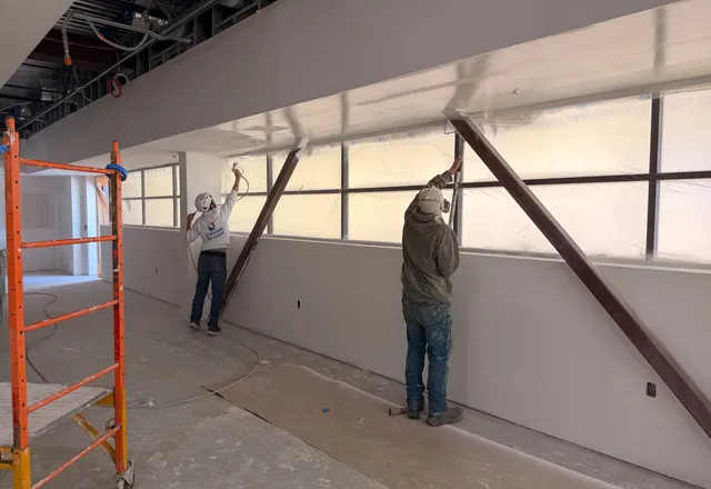 Two painters working on a freshly primed interior wall, one wearing a respirator