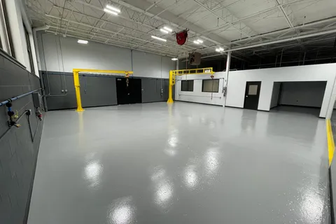 Shop bay with a glossy gray epoxy floor and yellow overhead cranes