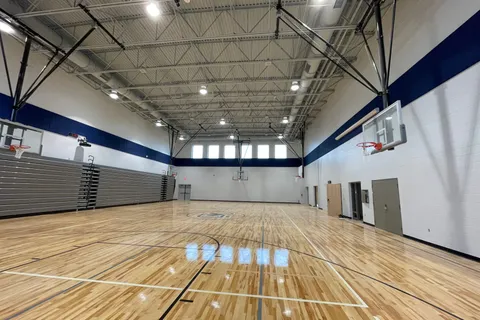 Finished gymnasium with a polished maple court, painted navy accent band, and steel roof trusses