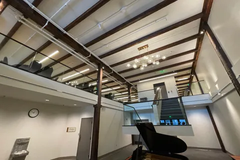 Lobby with exposed wood beams, a glass-railed mezzanine, and a grand piano