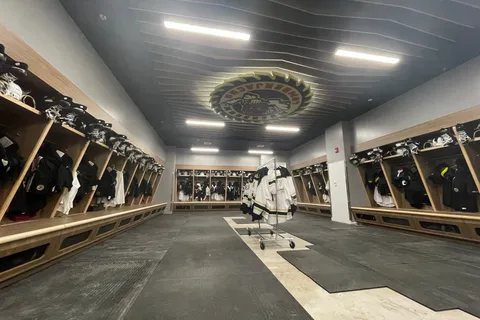 Hockey locker room with wood stalls, a painted dark ceiling, and a team logo at center