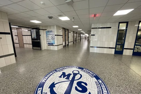 School hallway with a terrazzo-style floor featuring a school emblem and painted navy and white walls