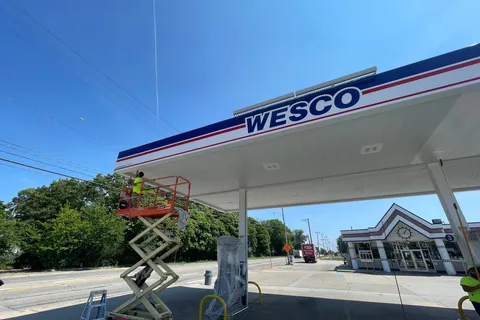 Fuel station canopy with a Wesco sign and a painter working from a scissor lift